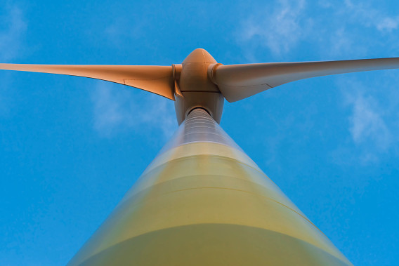 view from the ground up of a white windmill. The sky behind it is blue.