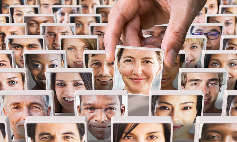 A collage of diverse faces, each framed individually, with a hand selecting one portrait of a smiling woman among them.